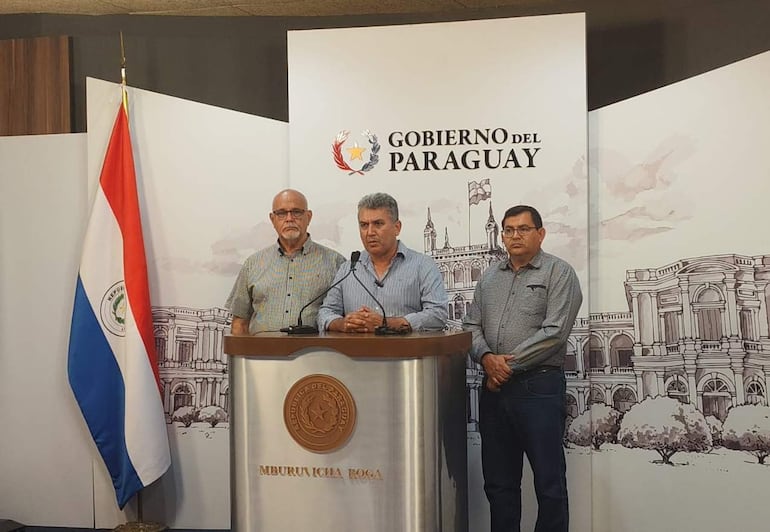 Silvio Piris y Rafael Resquín en camisas a cuadros, con expresiones serias, durante la presentación en un fondo con logos oficiales.