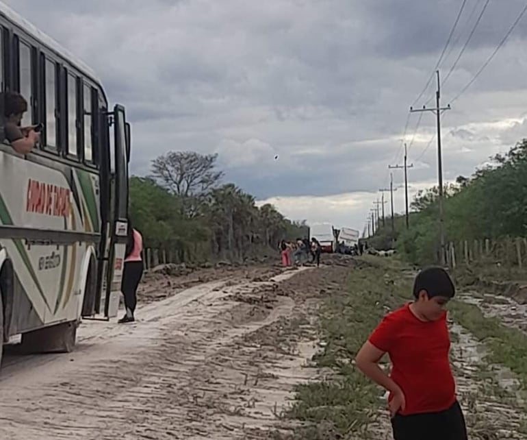 Un niño con camiseta roja observa en tierra, mientras un autobús se detiene y personas conversan a su alrededor.