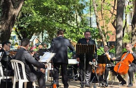 Grupo de músicos en trajes oscuros, con un cantante al micrófono y un pianista en teclado, rodeados de un entorno natural.