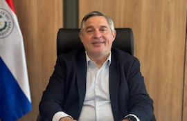Luis Ramírez, hombre de mediana edad con cabello canoso y blazer oscuro, revisa documentos en su oficina con la bandera de Paraguay de fondo.