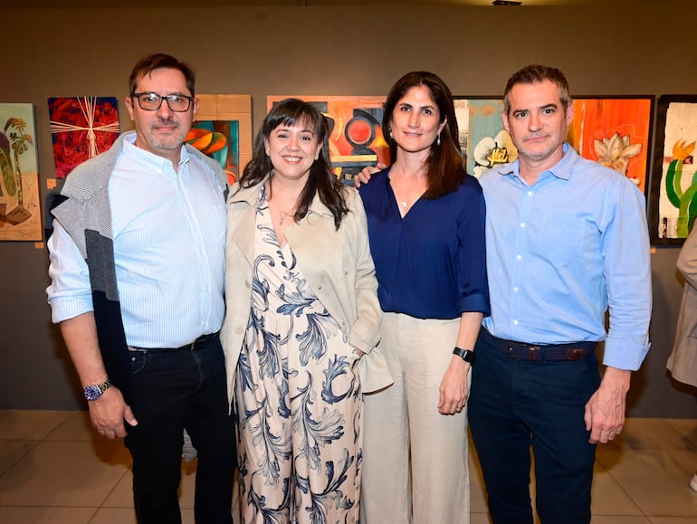 Dos hombres y dos mujeres, uno con camisa clara, conversan en un ambiente de galería de arte moderno y bien iluminado.