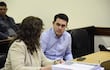 Hernán Rivas en chaqueta clara, sentado junto a un hombre de camisa de cuadros. Mesas con documentos y un teléfono móvil están visibles.