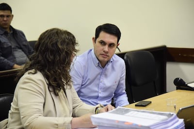 Hernán Rivas en chaqueta clara, sentado junto a un hombre de camisa de cuadros. Mesas con documentos y un teléfono móvil están visibles.