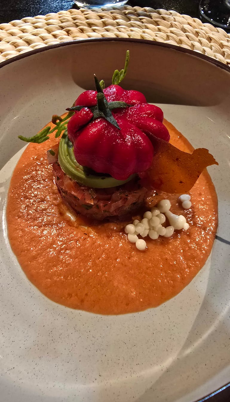 Plato con tomate rojo y guarnición en elegante vajilla dentro de un restaurante, sin personas presentes.