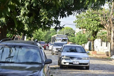 Calle empedrada con árboles y vehículos, incluyendo un autobús en dirección contraria. Ambiente urbano y tranquilo.