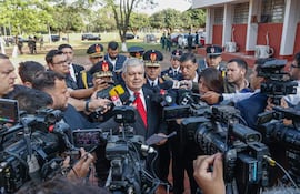 Enrique Riera con corbata roja habla a los periodistas rodeado de oficiales en un evento oficial al aire libre.