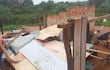 Hombre con camiseta roja trabajando en la estructura dañada, con madera y chapas esparcidas en un entorno rural.