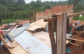 Hombre con camiseta roja trabajando en la estructura dañada, con madera y chapas esparcidas en un entorno rural.