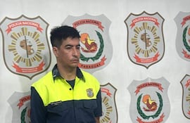 Hombre en uniforme de policía con expresión seria, frente a una pared con escudos de la Policía Nacional de Paraguay.