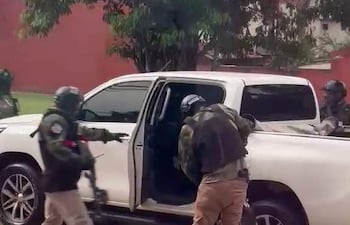 Tres agentes tácticos en movimiento cerca de una camioneta blanca, con cascos y ropa especializada, en un área urbana.