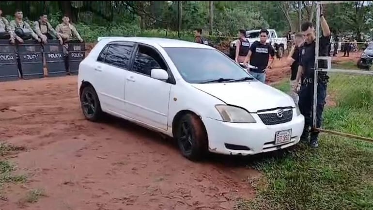 Automóvil blanco detenido por la policía en control de seguridad, con agentes supervisando en un entorno de vegetación.