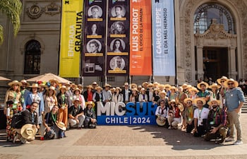 Grupo de personas, mayoría con sombreros, sonríen en evento al aire libre, posando frente al museo con lema de MICSUR 2024.