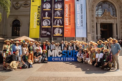 Grupo de personas, mayoría con sombreros, sonríen en evento al aire libre, posando frente al museo con lema de MICSUR 2024.