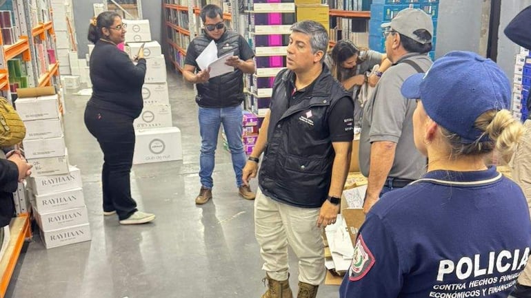 Mujer de espaldas observa a un hombre con documento mientras policías revisan cajas en un almacén bien iluminado.
