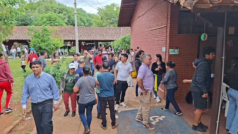 Grupo de personas conversando en un ambiente exterior, con un hombre de camisa clara y pantalones oscuros al frente en medio de la reunión.