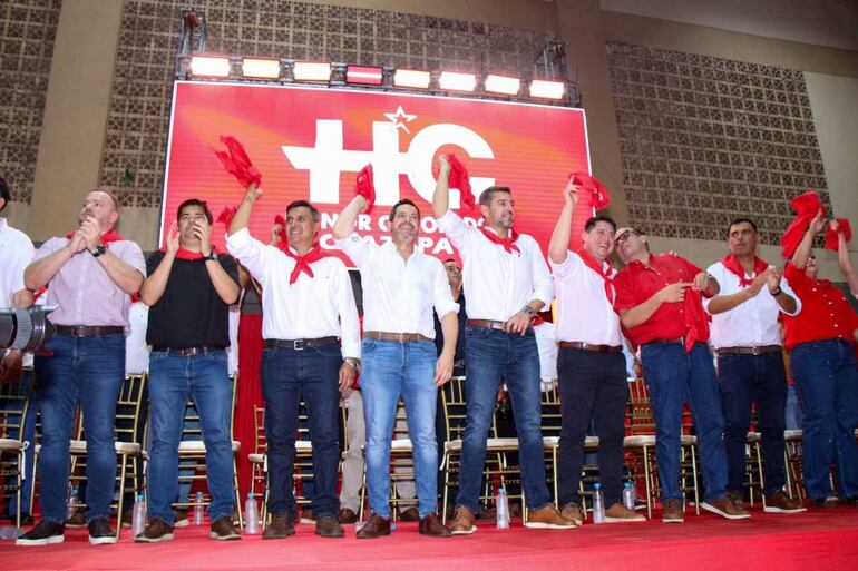 Alliana y Latorre en tarima, vistiendo camisetas blancas y pantalones oscuros, celebran con pañuelos rojos.