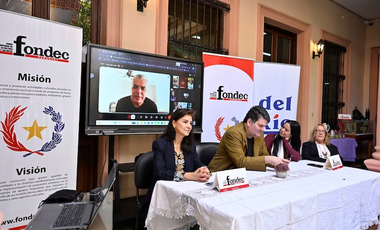Mujer de blusa clara en el centro observa el monitor. Dos mujeres a la derecha y un hombre escribiendo a la izquierda, en un salón iluminado.