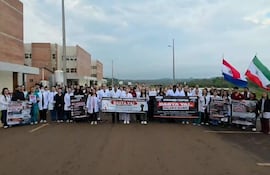 Grupo de médicos con batas blancas sostiene pancartas con mensajes de reivindicación, frente a un hospital, en una vibrante protesta.