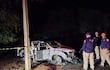 Cuatro personas, tres policías en uniforme, observan un vehículo dañado por el fuego en un ambiente rural oscuro.