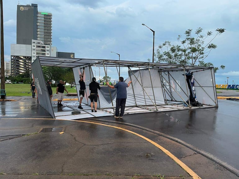 Varias personas manipulando una estructura metálica volcada en un entorno urbano, con clima nublado y suelo mojado.