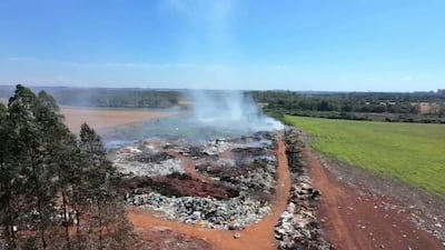 Basural en llamas en Campo 9, con humo denso y árboles a la izquierda, en un día soleado.