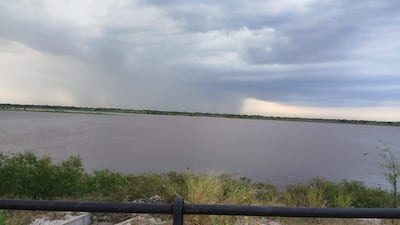 Nubes grises y cielo amenazante sobre un cuerpo de agua, con vegetación al lado, anunciando una posible tormenta.