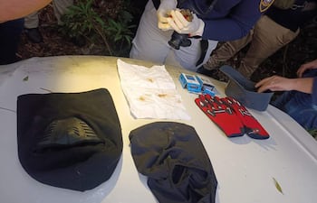 Agentes en ropa táctica y guantes recogen evidencias en un entorno boscoso junto a un vehículo blanco.