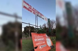 Valla publicitaria de Valeria Romero y Rigo Chamorro en entorno deportivo, rodeada de vegetación.