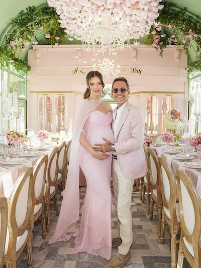 Nadia Ferreira en vestido rosa claro y Marc Anthony en traje claro sonríen abrazados en un evento decorado elegantemente.