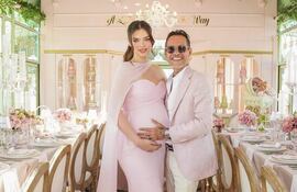 Nadia Ferreira en vestido rosa claro y Marc Anthony en traje claro sonríen abrazados en un evento decorado elegantemente.