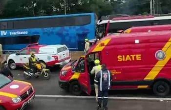 Camioneta roja del SIATE y ambulancia en escena del accidente, con un autobús azul dañado y rescatistas preparando atención.