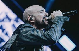Abel Pintos con chaqueta de cuero y micrófono, expresa emociones intensas mientras canta en un escenario iluminado.