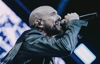 Abel Pintos con chaqueta de cuero y micrófono, expresa emociones intensas mientras canta en un escenario iluminado.