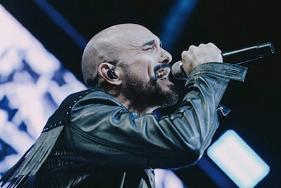 Abel Pintos con chaqueta de cuero y micrófono, expresa emociones intensas mientras canta en un escenario iluminado.