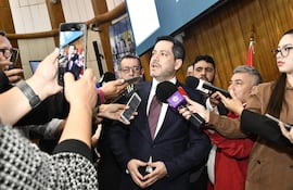 Raúl Latorre en traje oscuro en medio de periodistas que le hacen preguntas, rodeado de un ambiente formal con decoración de madera.