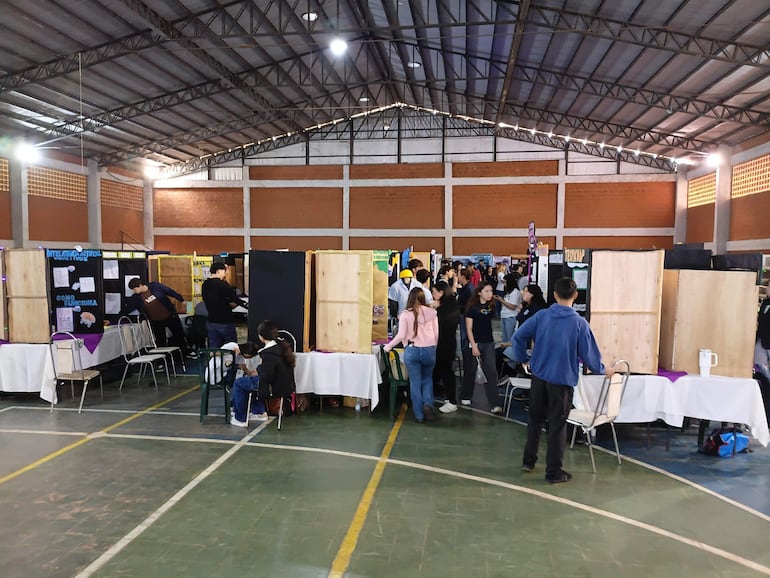 Estudiantes interactuando en el evento, con mesas decoradas y carteles sobre inteligencia artificial en un ambiente dinámico.