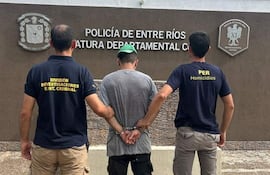 Detenido Nicolás Alexander Acosta esposado, rodeado de agentes de policía con camisetas oscuras frente a cartel de Jefatura Departamental Colón.