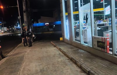 Dos policías en uniforme conversan frente a un escaparate roto en una calle de Villa Elisa, con un negocio Grido iluminado al fondo.