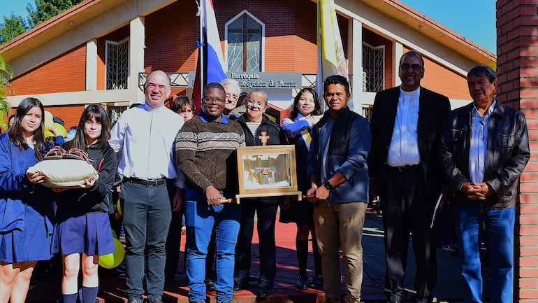 Hombres y mujeres en el exterior de la parroquia, algunos en sotanas y otros en uniformes escolares, sonríen alrededor de la reliquia de San Francisco de Asís.
