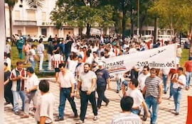 Hombre con altavoz lidera protestas de personas con camisetas diversas y banderas paraguayas en una manifestación.