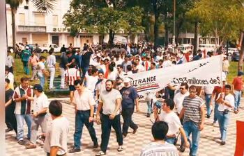 Hombre con altavoz lidera protestas de personas con camisetas diversas y banderas paraguayas en una manifestación.