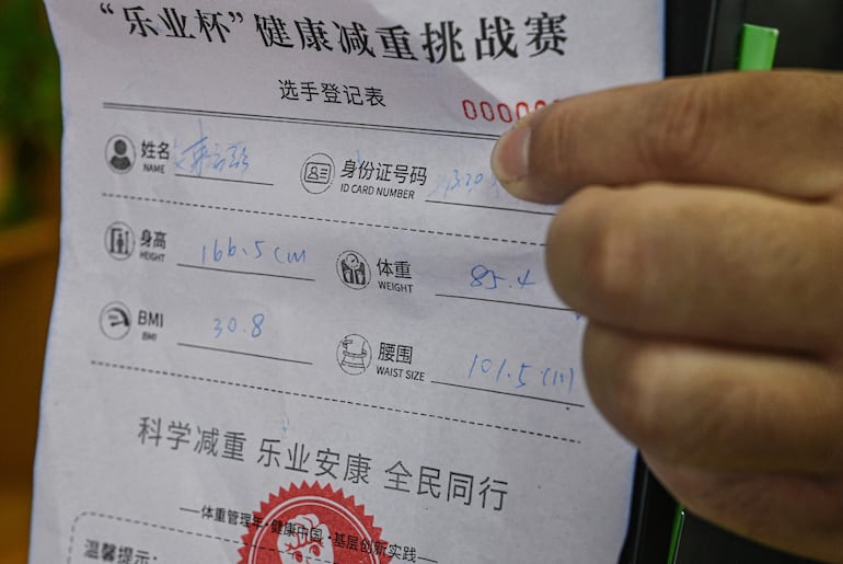 La fotografía tomada el 23 de marzo de 2026 muestra a un participante masculino sosteniendo un formulario de inscripción que exhibe sus medidas corporales en un centro comunitario local en Wuxi, en la provincia de Jiangsu, en el este de China.