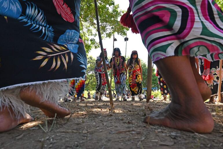 Mujeres del Pueblo Maka visten trajes coloridos y accesorios culturales, participando en danza al aire libre entre árboles.