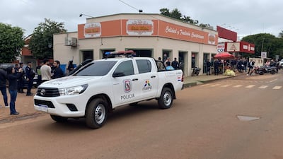 Camioneta policial en primer plano con distintivos, personas en el fondo, un día nublado que agrega tensión a la escena.
