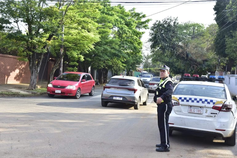 Agente de policía en uniforme dirigiendo el tráfico en una calle congestionada, con varios vehículos y vegetación a los lados.
