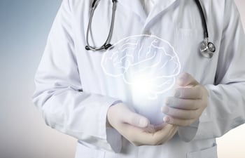Un profesional de la salud con bata blanca y un estetoscopio alrededor del cuello con la imagen de un cerebro dibujada entre las manos.
