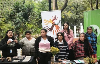 Grupo de ocho mujeres, algunas con collares y suéteres, dialogan en un entorno natural rodeadas de vegetación y artesanías.