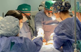 Seis profesionales de la salud en quirófano, vestidos con batas y mascarillas, proceden con cirugía reconstructiva en ambiente hospitalario.