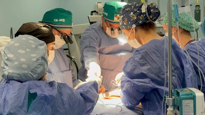 Seis profesionales de la salud en quirófano, vestidos con batas y mascarillas, proceden con cirugía reconstructiva en ambiente hospitalario.
