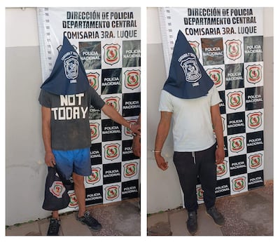 Dos hombres con gorras, uno en camiseta gris y pantalones cortos, sostienen una bolsa negra frente a la Comisaría 3ra de Luque.